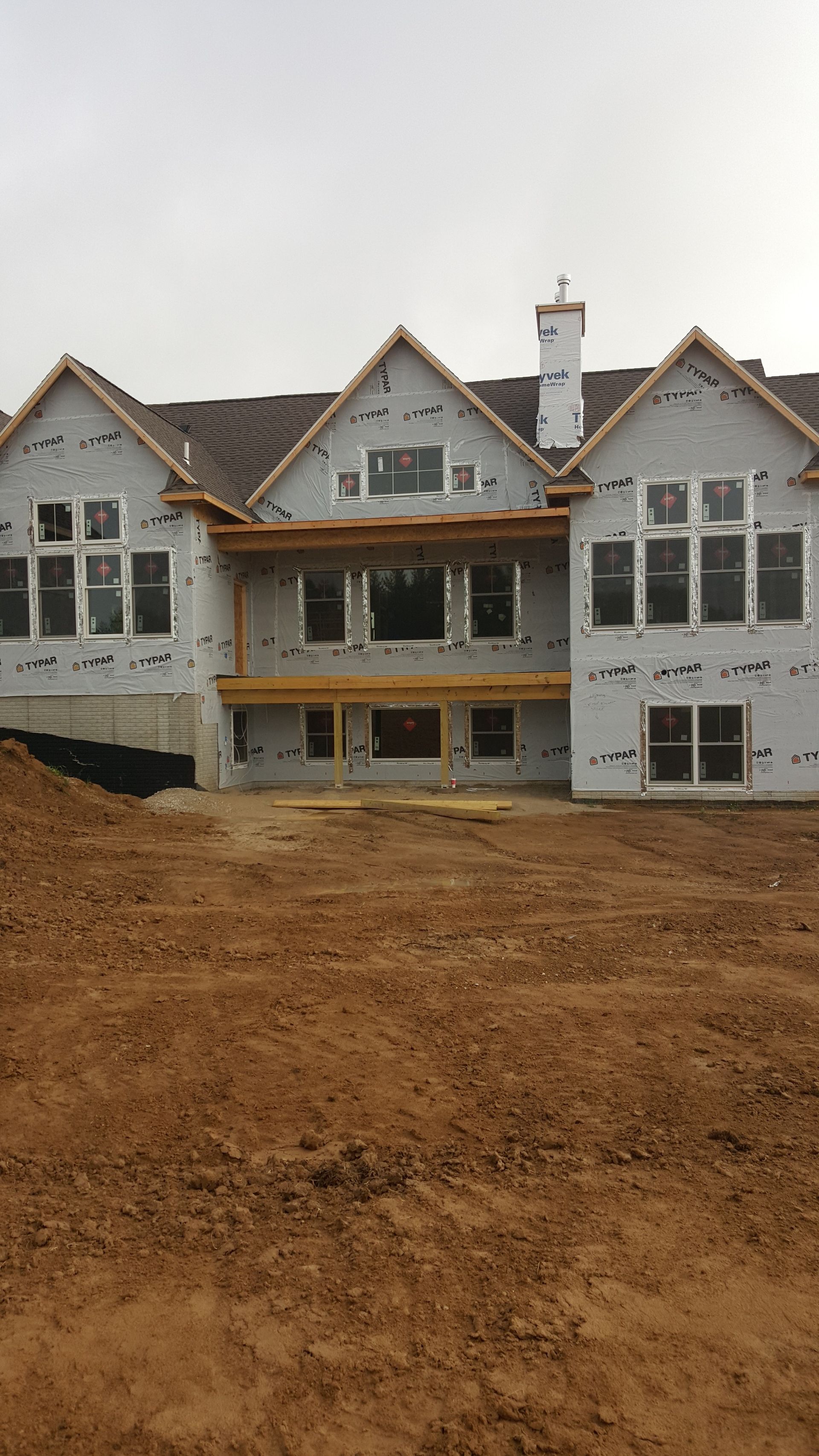Partially built row of white houses with gabled roofs on a dirt lot under an overcast sky