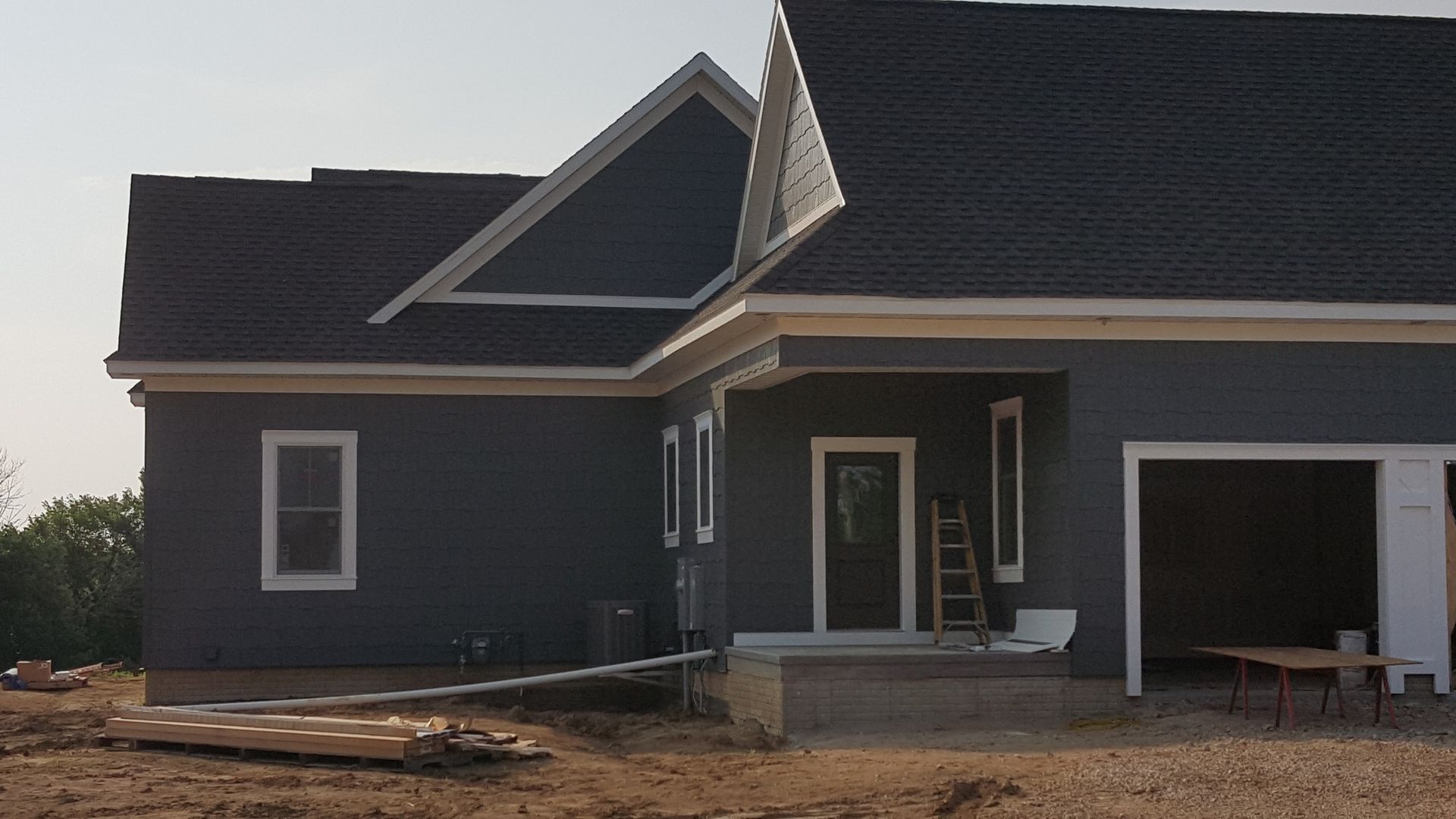 Dark gray house under construction with white trim and an open garage in front.