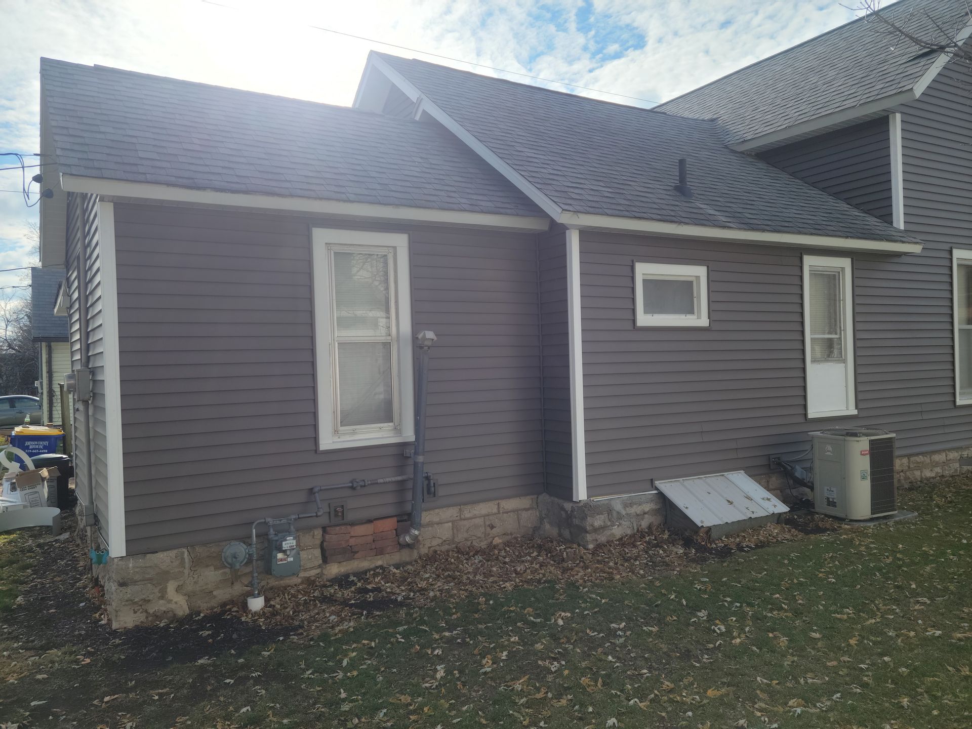 Gray house exterior with white-trimmed windows, sloped roof, and small yard with fallen leaves