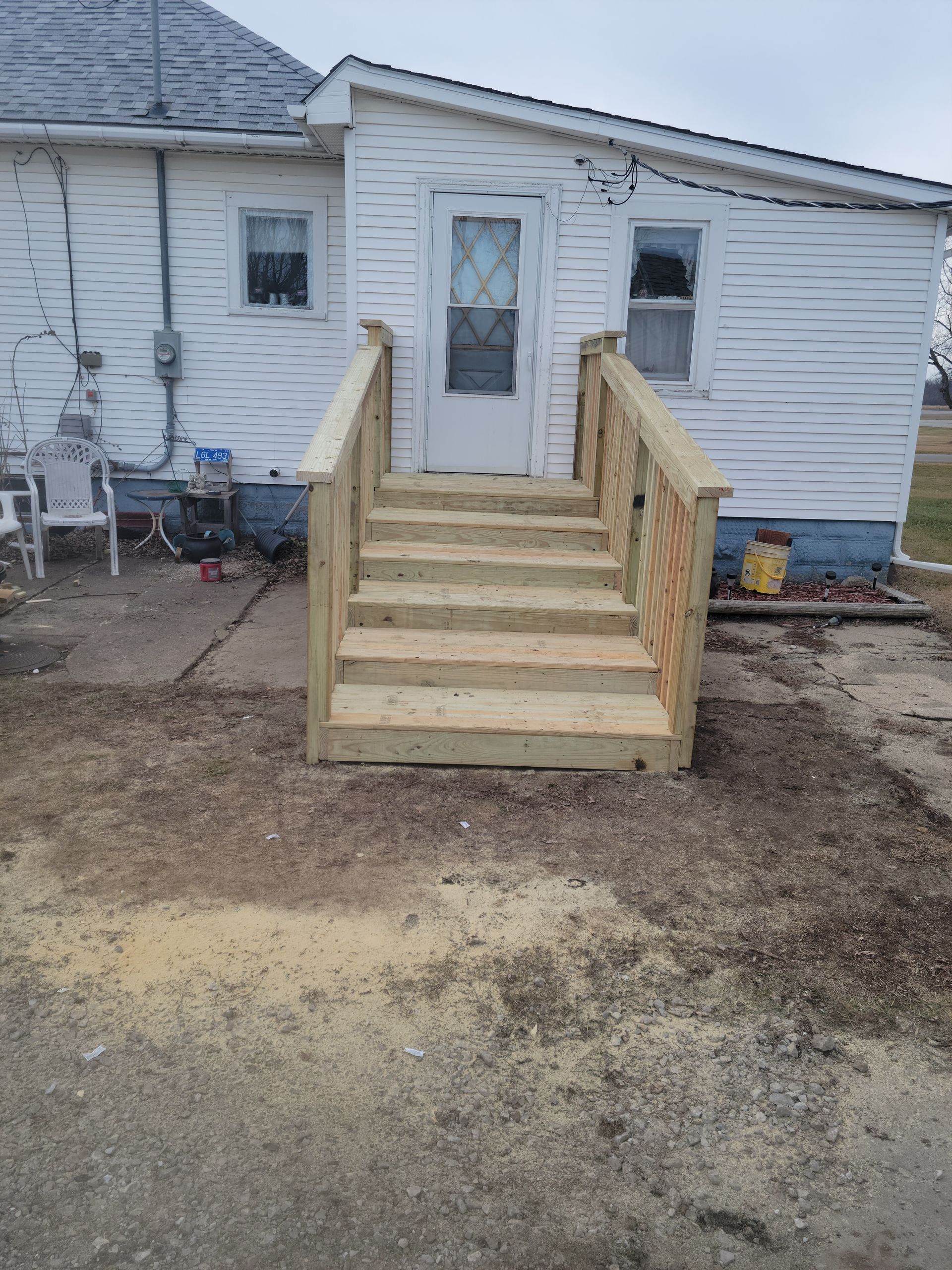 Wooden accessibility ramp leading to a white house door over a dirt yard