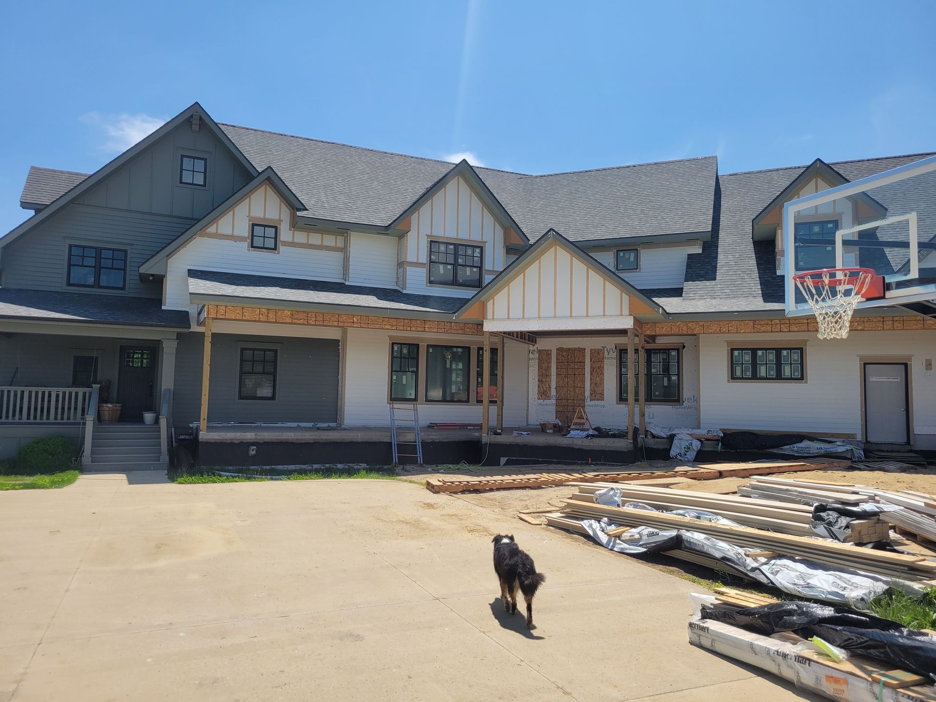 Large rustic house with a porch, basketball hoop, and a small dog in the driveway