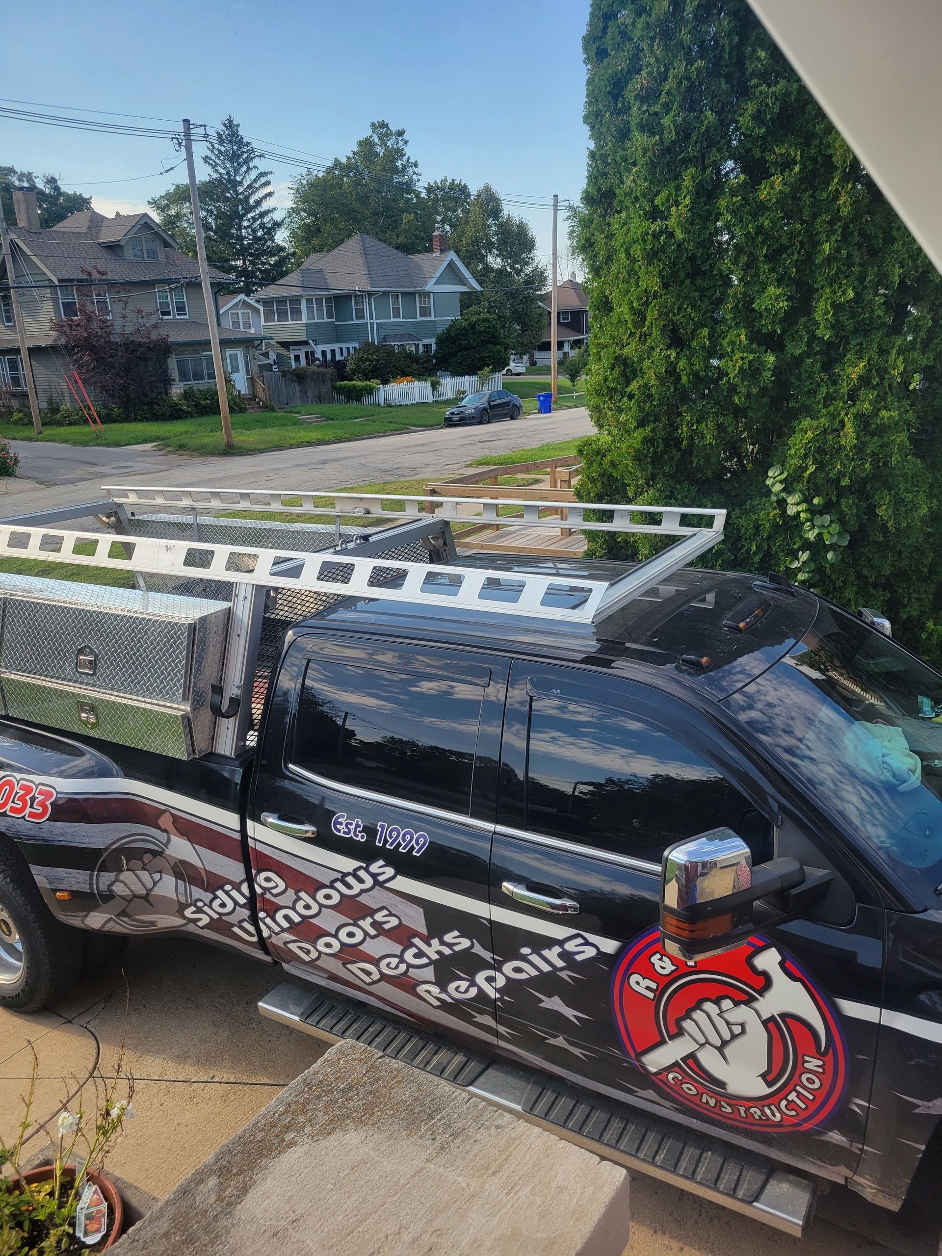 Black pickup truck with roof rack and decals parked on a residential street beside trees and houses