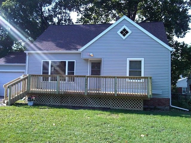 Blue house with a front porch and wooden deck, surrounded by grass and trees