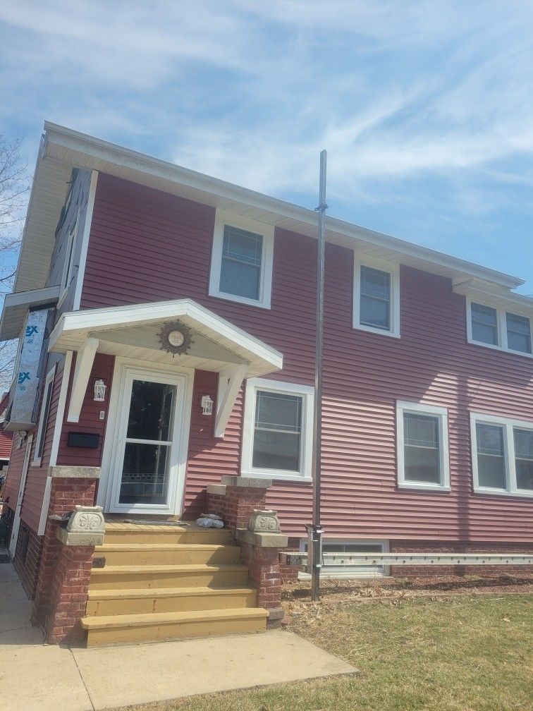Two-story red house with white trim, front steps, and small porch under a blue sky