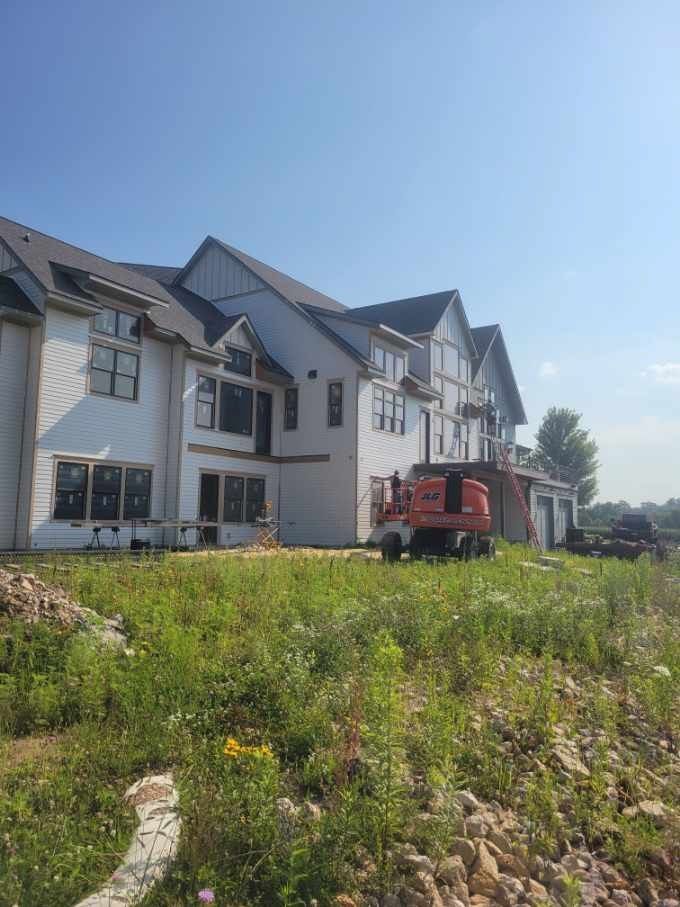 New house under construction with a red truck on a grassy hillside under a blue sky