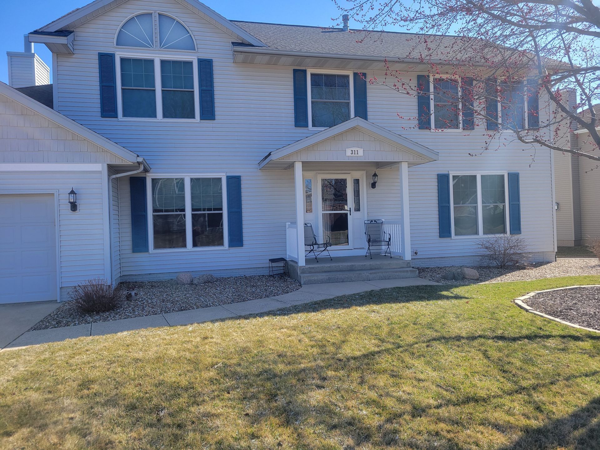 Two-story white suburban house with a front porch and green lawn under a clear blue sky