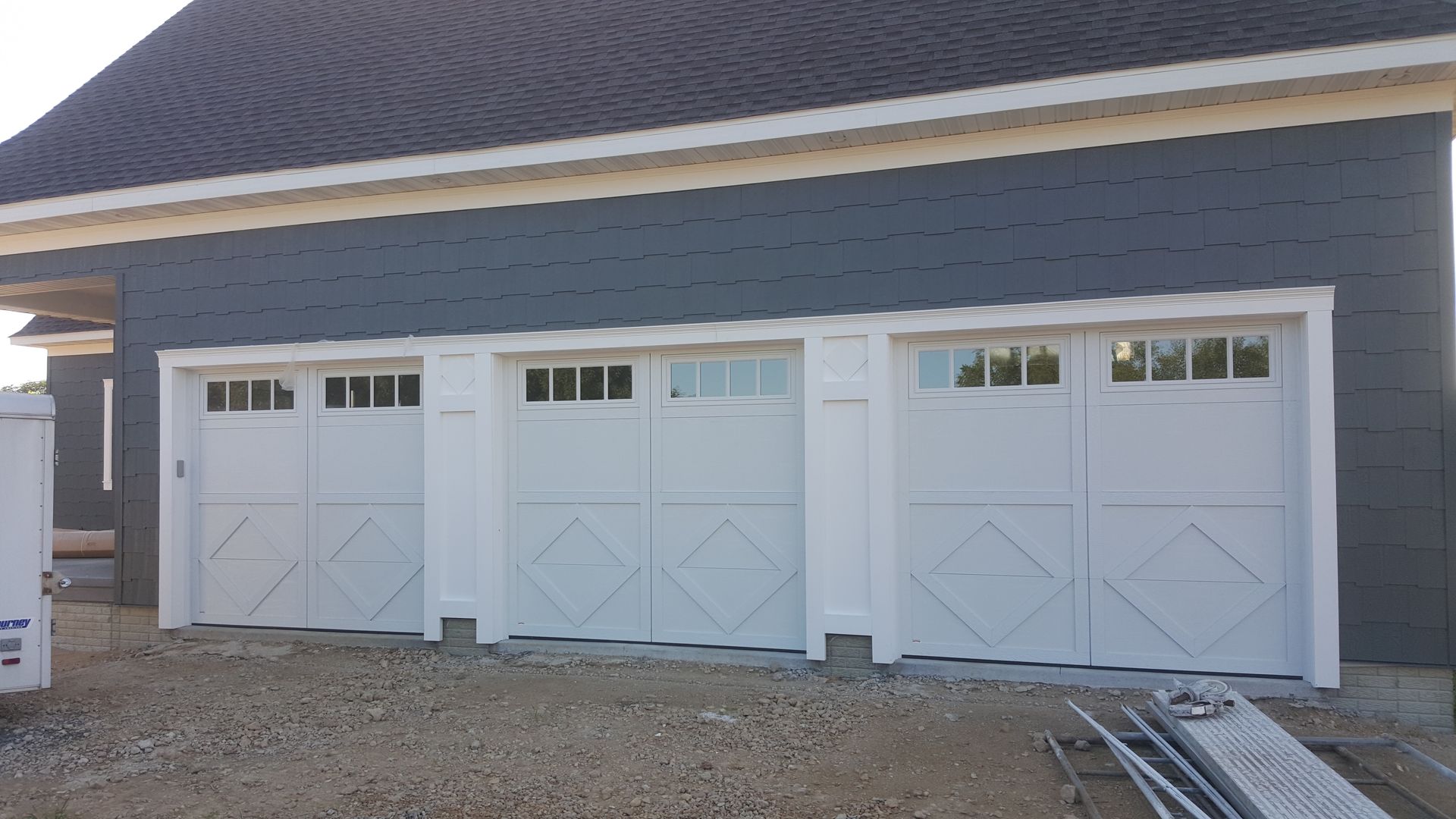 Four white garage doors on a blue-gray house exterior with stone accents and gravel foreground