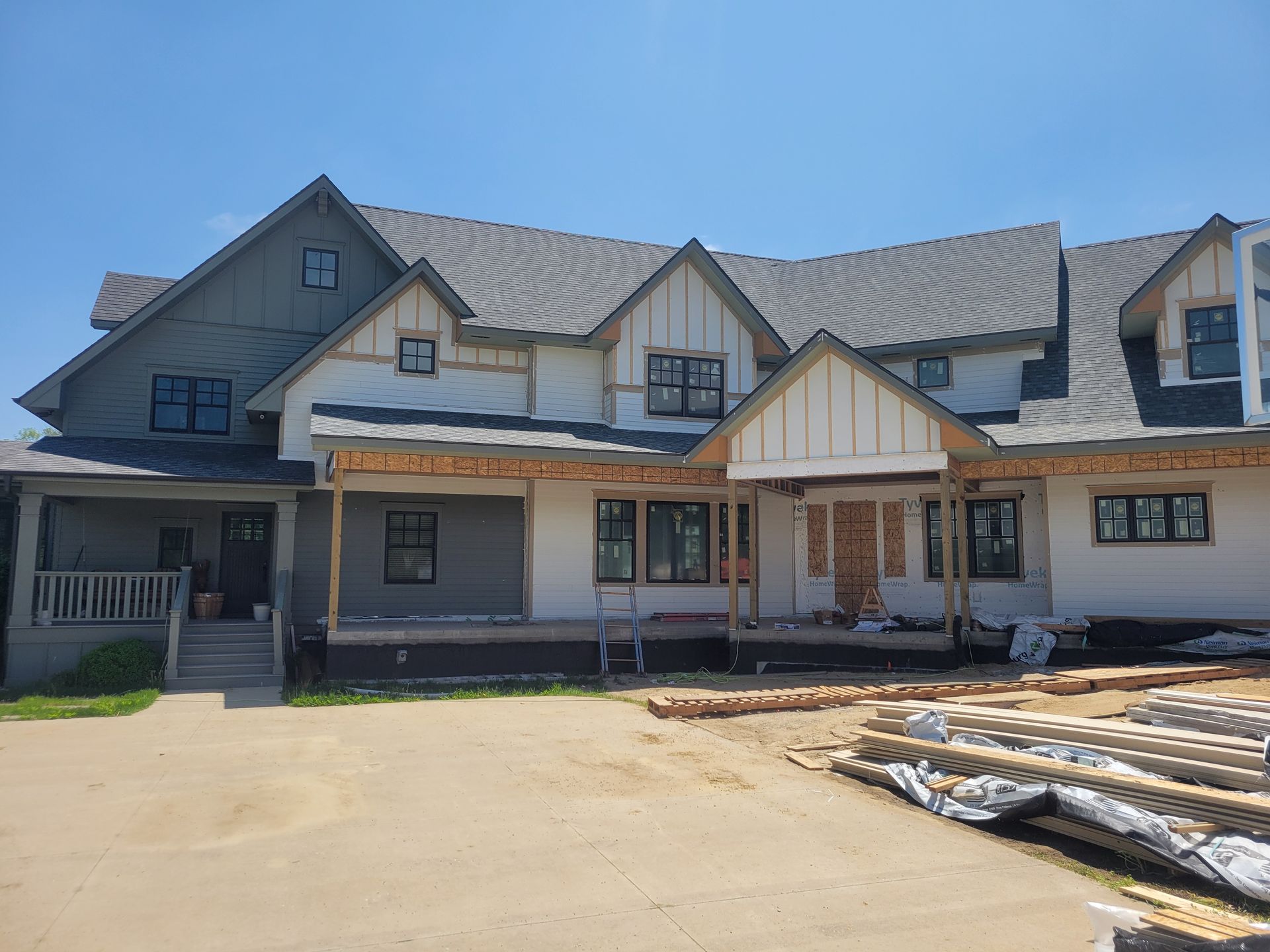 Exterior of a large house under construction with gray siding, a covered porch, and building materials in front