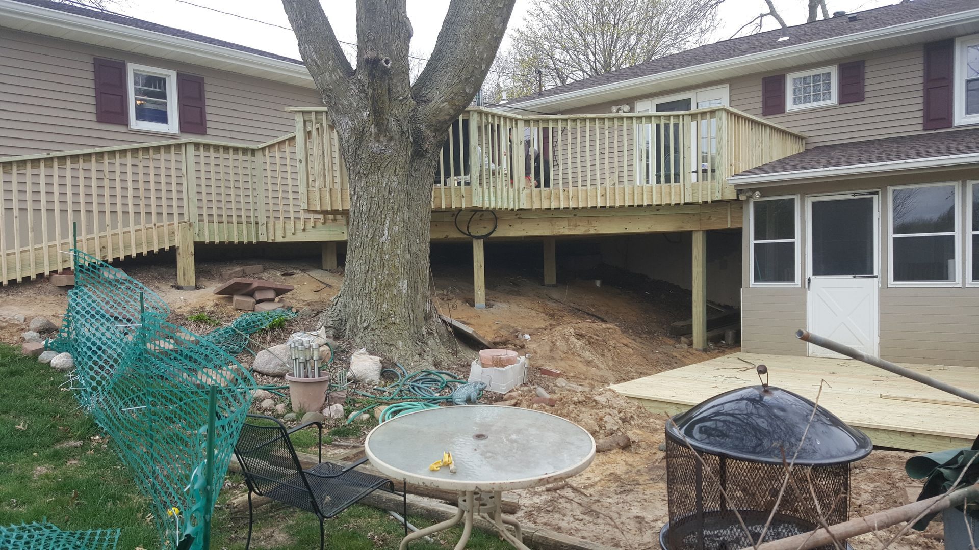 Backyard deck with a large tree, patio furniture, and a house with screened porch and railings