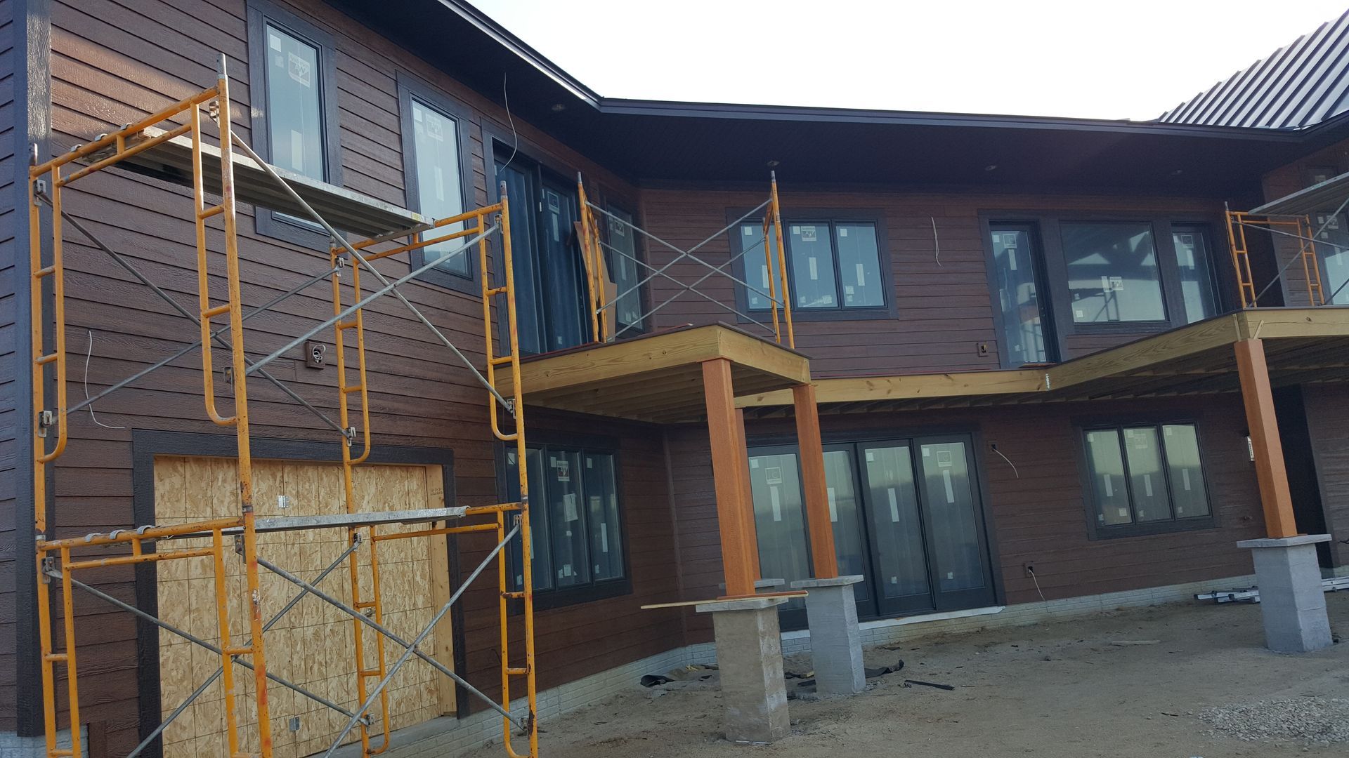 Two-story dark wood building under construction with orange scaffolding and concrete steps.