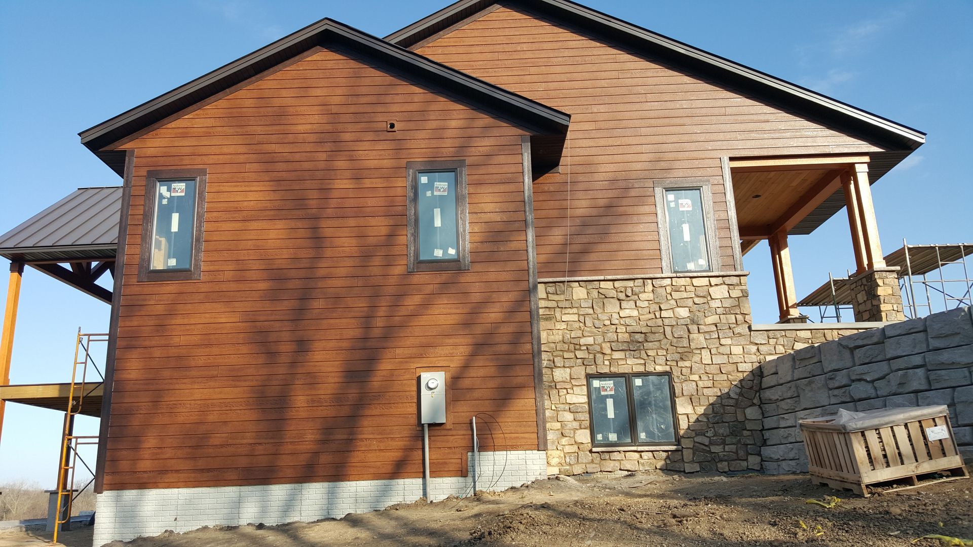 New two-story house with wood and stone exterior on a sloped lot, viewed from the side