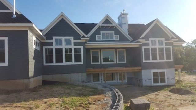 Gray house exterior with white trim and large windows, viewed from the front yard under bright sunlight