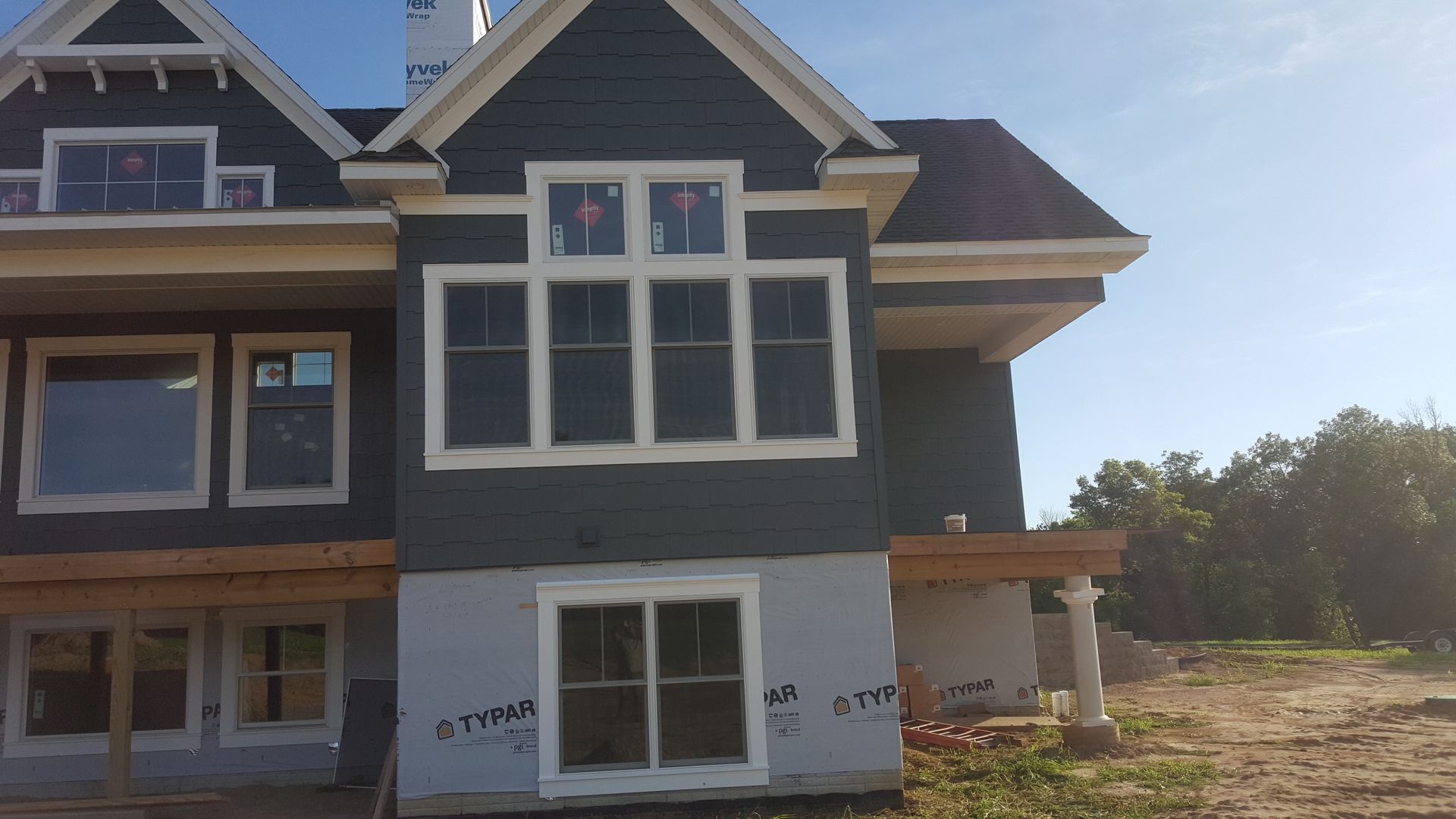 Partially built house exterior with gray siding, white trim, and unfinished landscaping under a clear sky