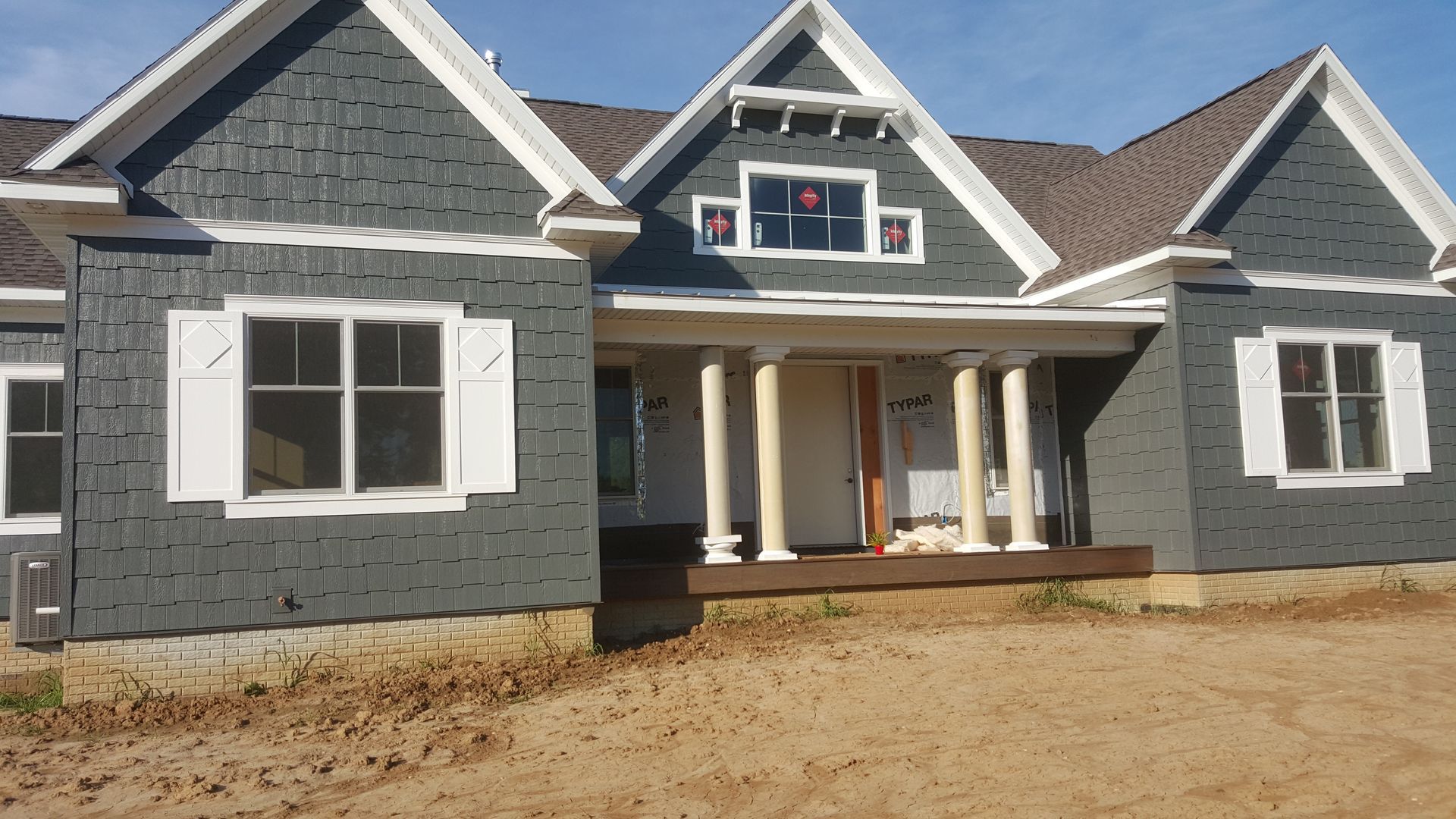 New gray house under construction with white trim and unfinished dirt front yard