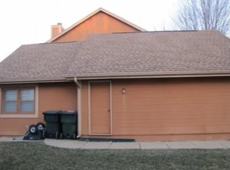 Orange house exterior with brown shingled roof and trash bins by the side wall