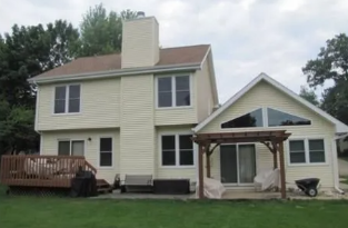 Two-story beige house with a deck, patio cover, and grassy yard under cloudy skies