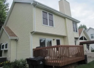 Two-story beige house with a wooden deck and sliding door in the backyard.