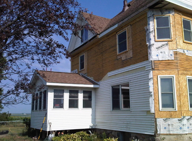 Old yellow house with white siding addition under a tree by open fields