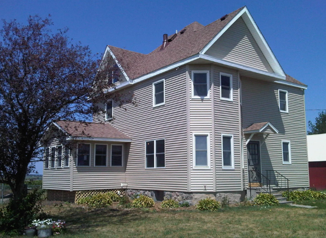 Beige two-story house with white trim and red roof, viewed from the front yard on a sunny day