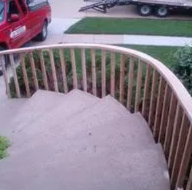 Curved concrete front steps with white railing beside a sidewalk and parked red vehicle