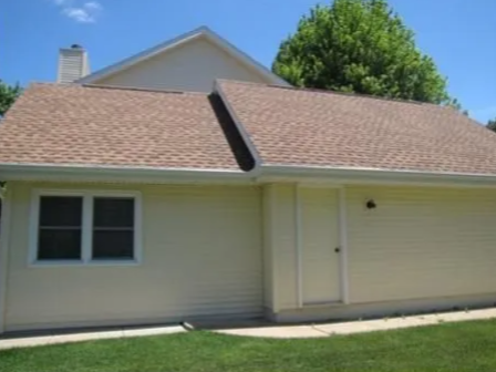 Single-story beige house with tan roof, white trim, and a front door under a blue sky.