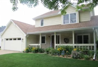 Two-story suburban house with white porch, attached garage, and well-kept front lawn