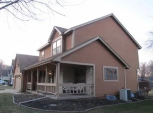 Two-story brown house with a covered front porch and gabled roof on a cloudy day