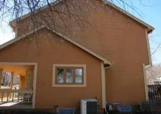 Two-story tan house with a small porch, windows, and bare tree branches overhead