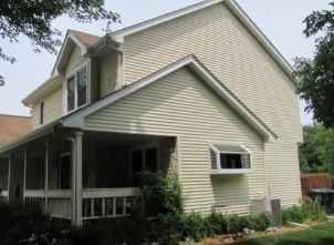 Beige two-story house with a covered porch and small front garden, viewed from the yard.