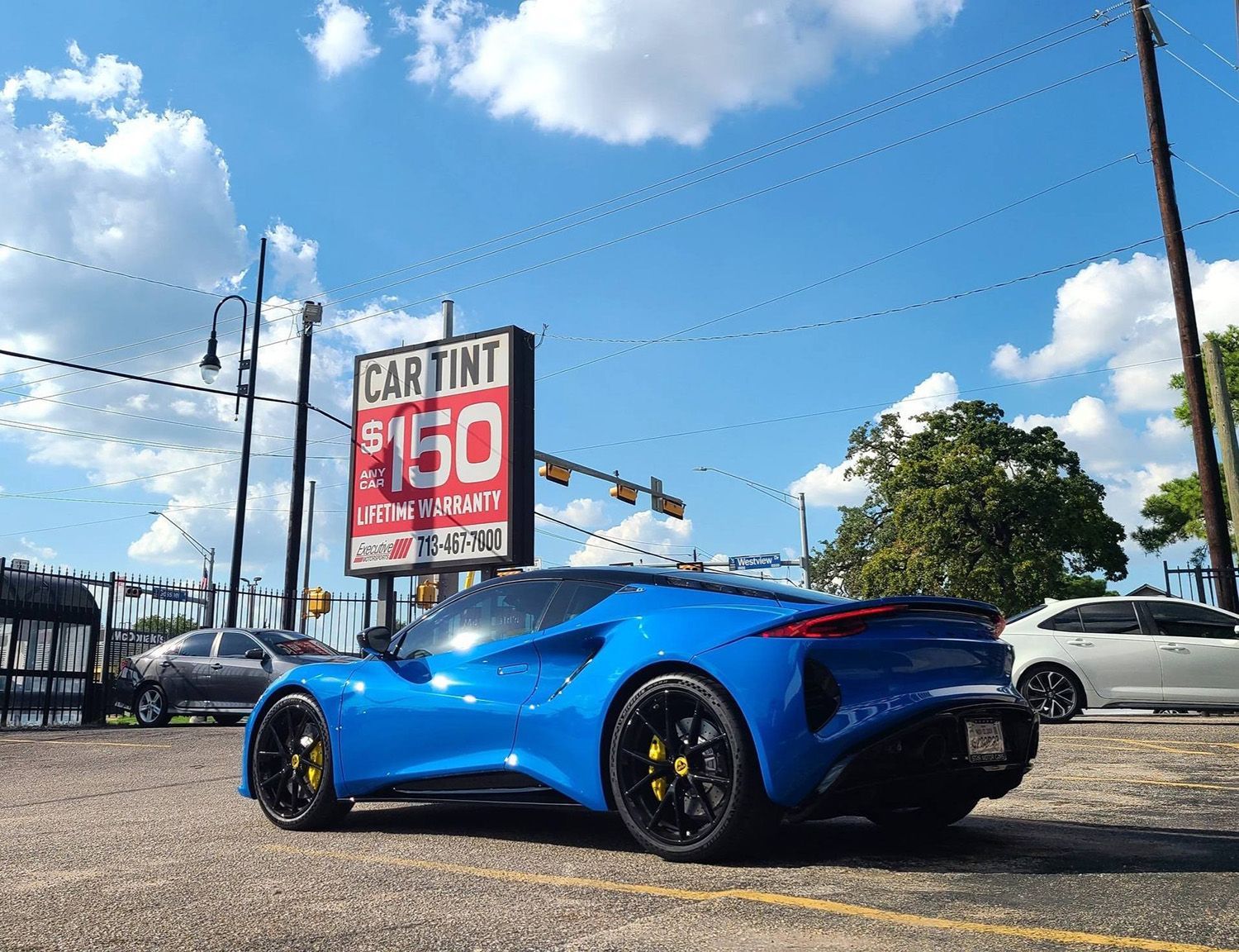 A blue sports car is parked in a parking lot in front of a car tint sign.