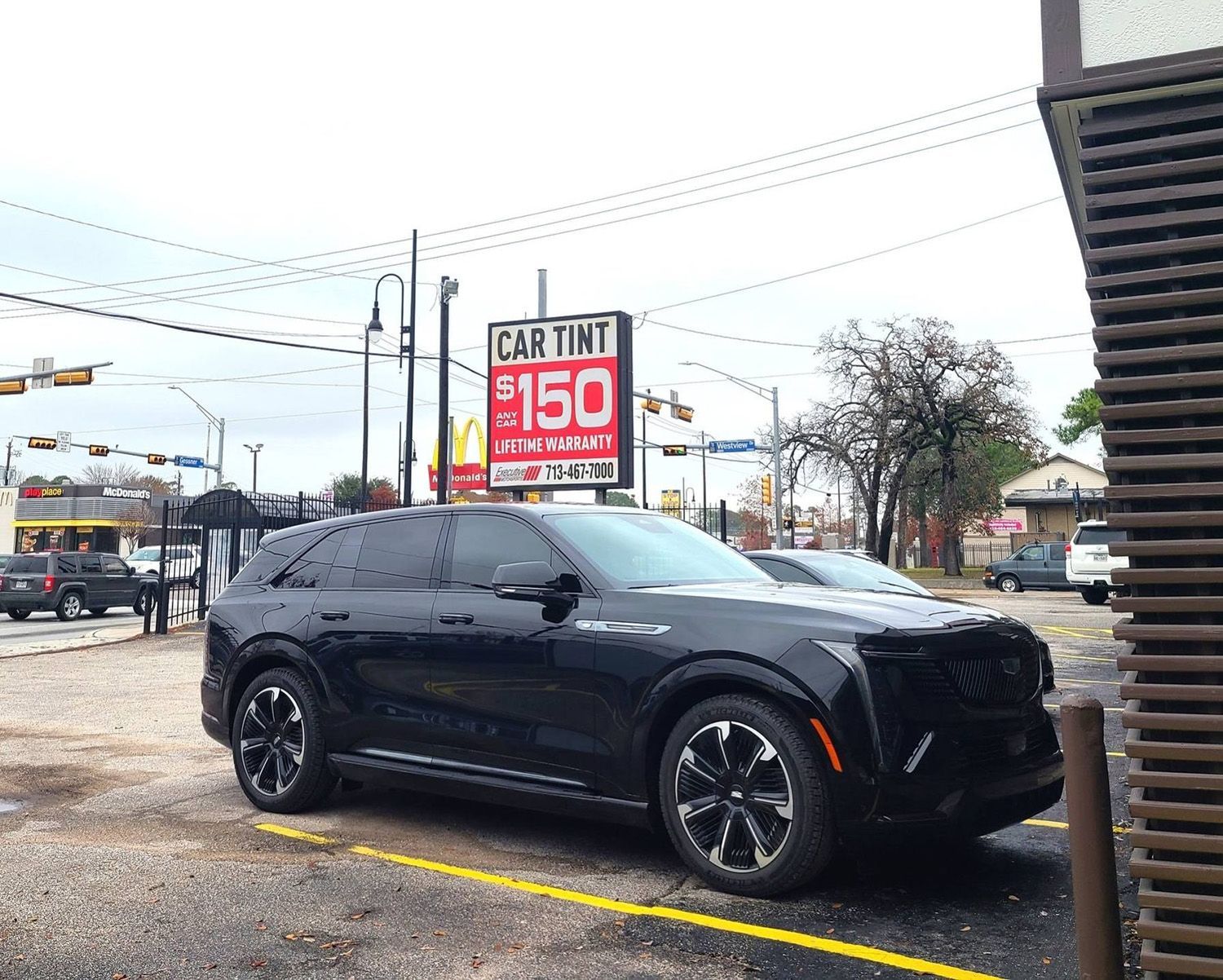 A black car is parked in a parking lot in front of a car tint sign.