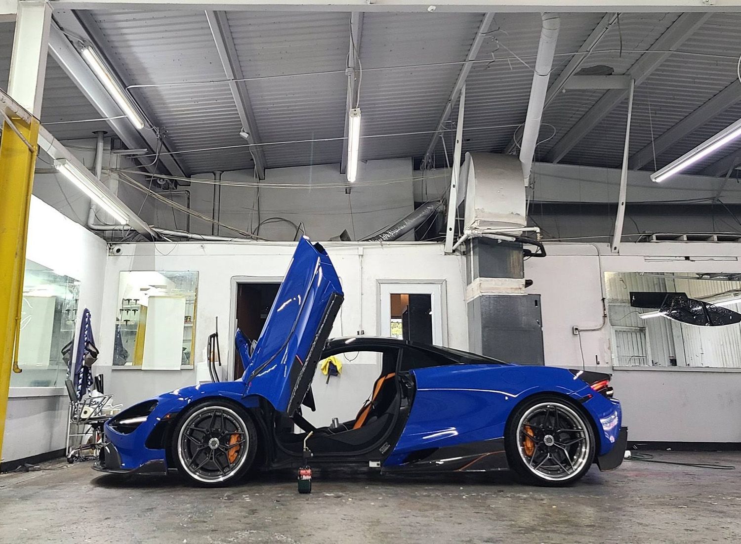 A blue sports car is parked in a garage with its hood open.