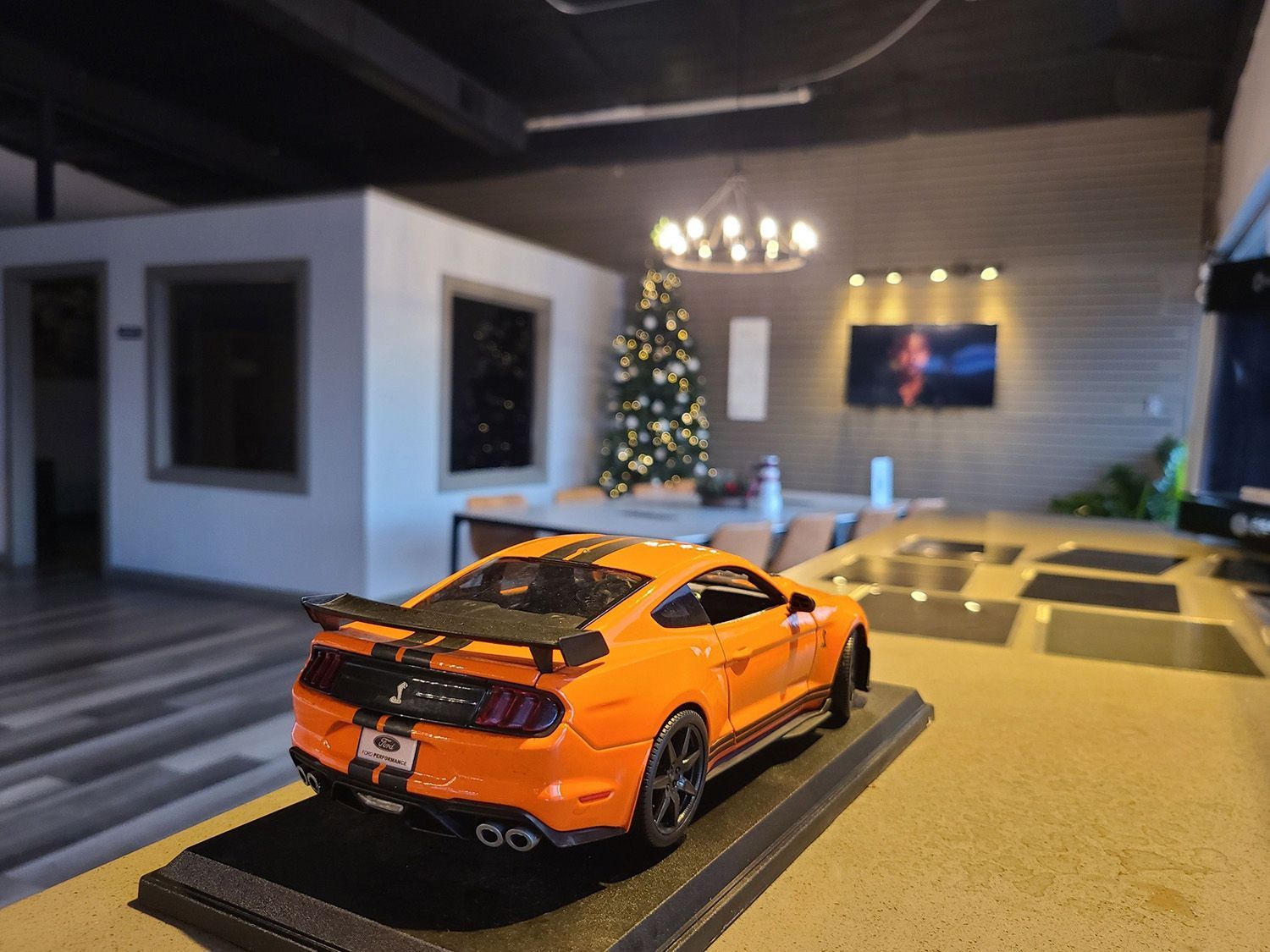 A model car is sitting on a counter in a living room with a christmas tree in the background.