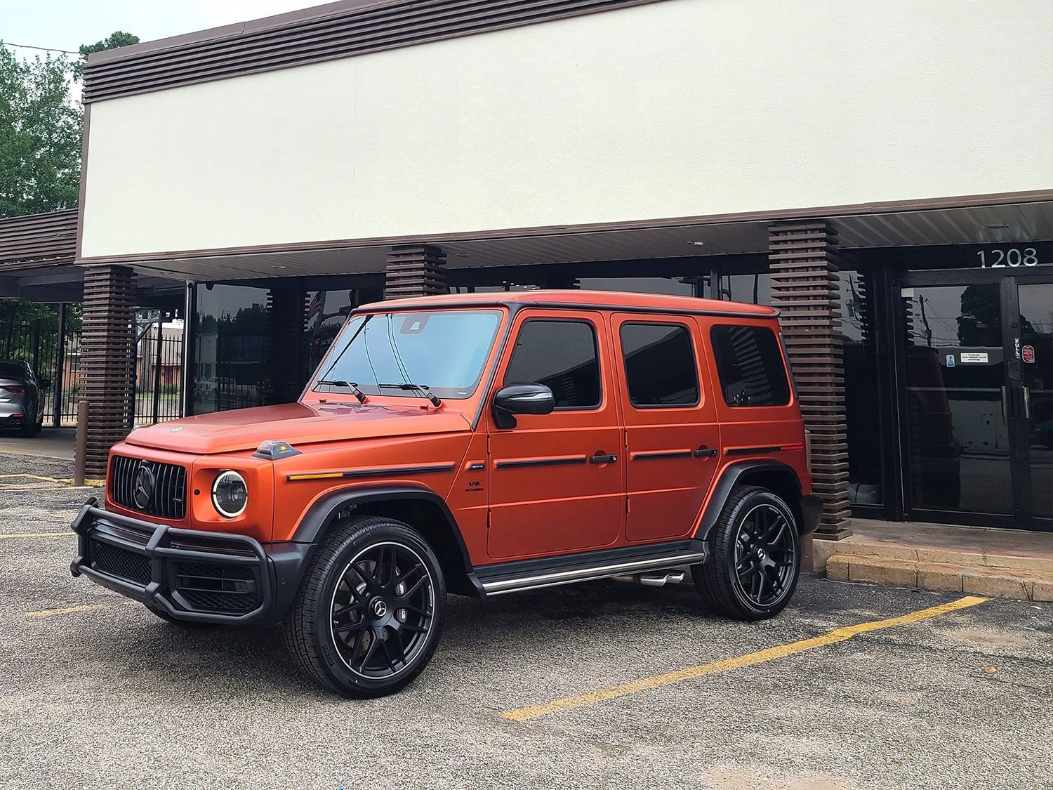 A red mercedes benz g63 is parked in front of a building.
