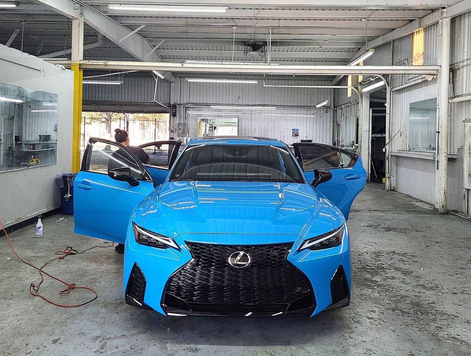 A blue lexus is parked in a garage with its doors open.