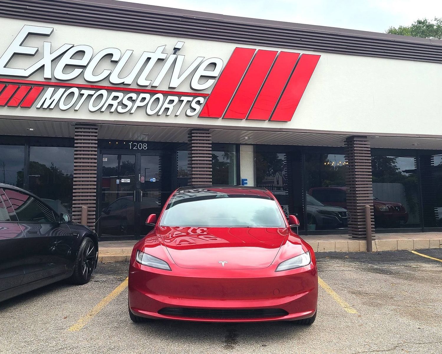 A red Tesla is parked in front of the shop