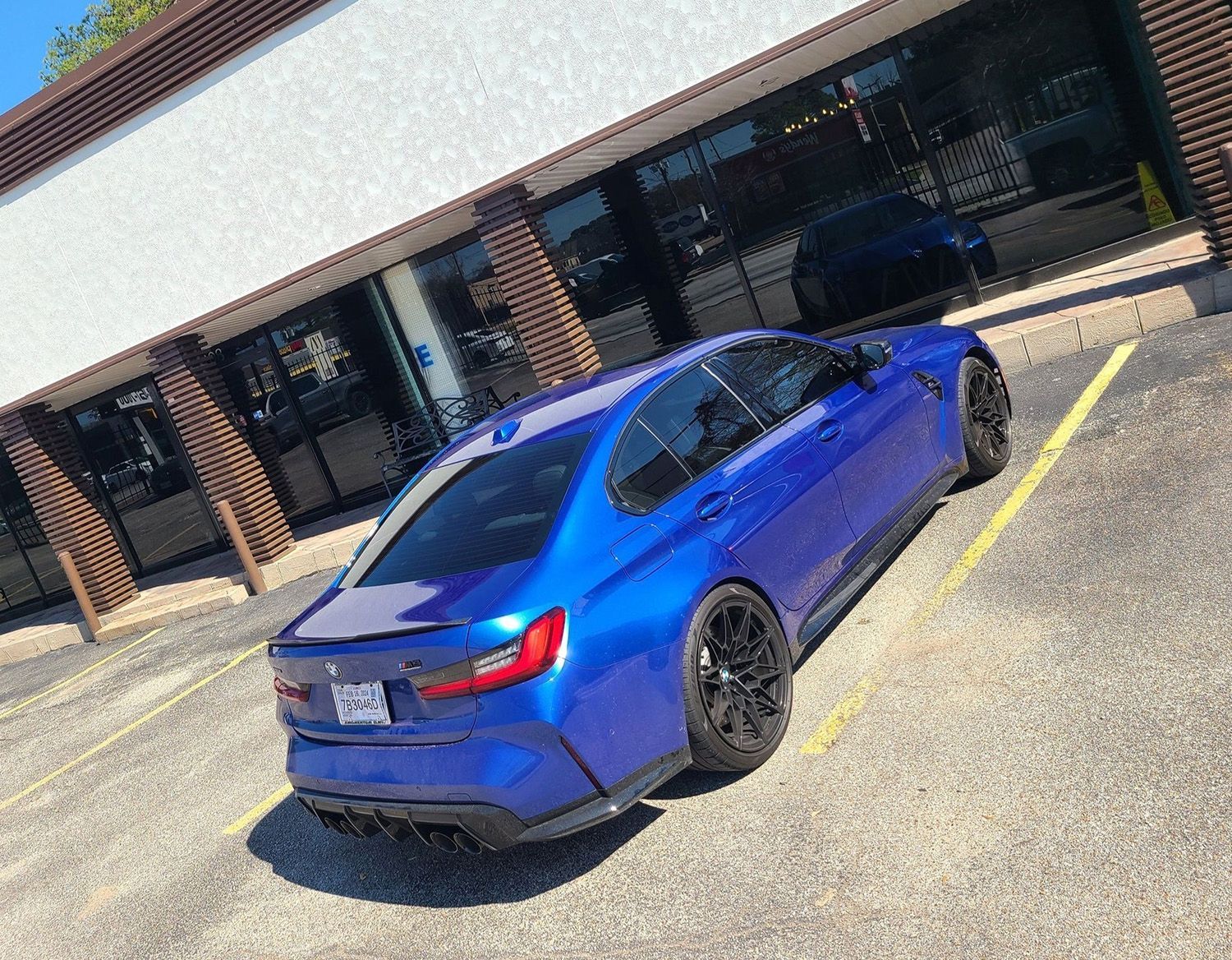A blue BMW is parked in a parking lot in front of a building.