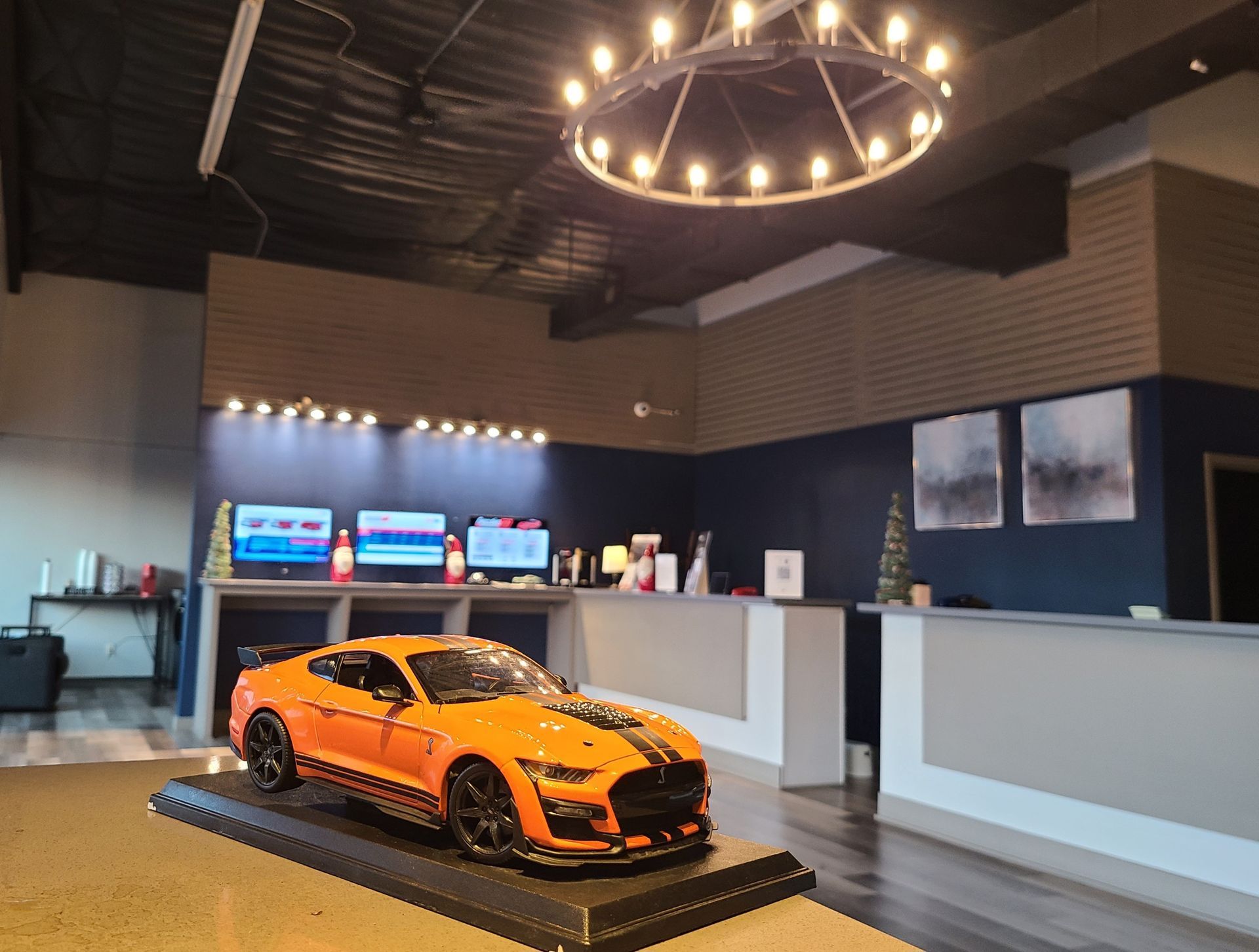 Orange sports car display in a modern showroom with a reception counter and hanging ring light