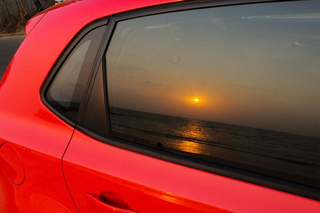 Sunset reflected in a car window on a red vehicle by the water