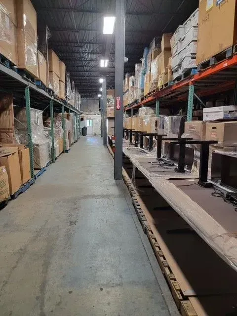A narrow warehouse aisle with stacked boxes and shelves on both sides.