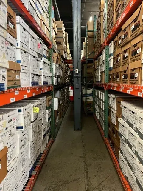 Narrow warehouse aisle lined with stacked boxes and shelves on both sides