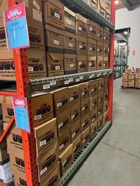 Warehouse aisle with stacked cardboard boxes on orange metal shelving and a concrete floor.