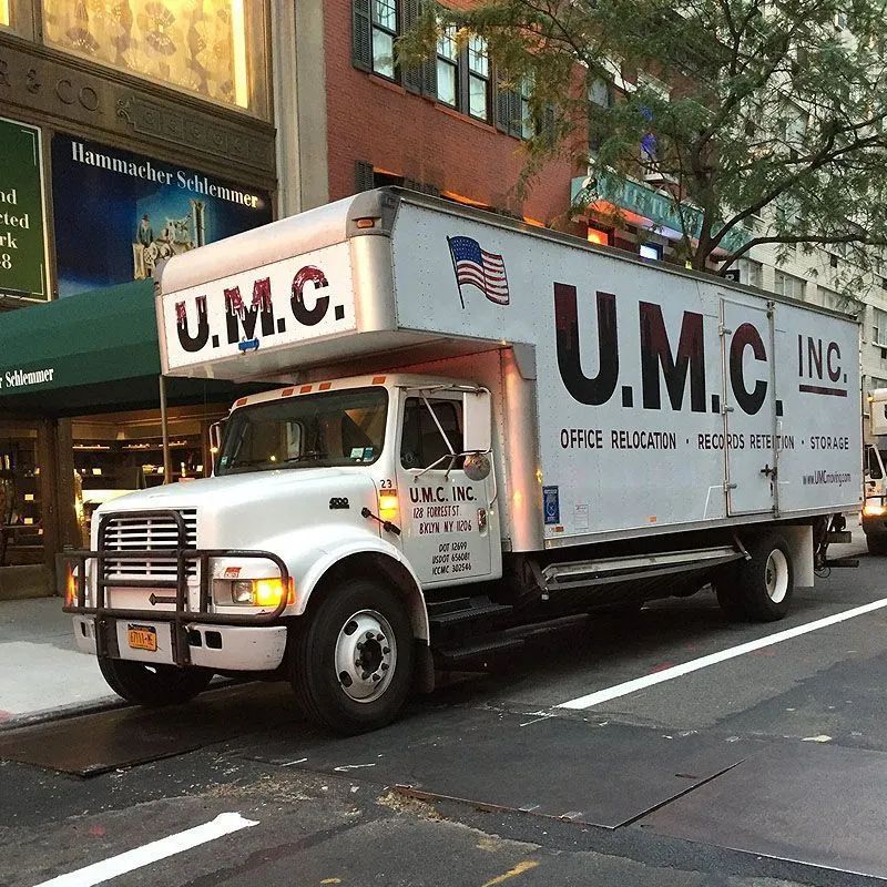 White U.M.C. moving truck parked on a city street beside a sidewalk