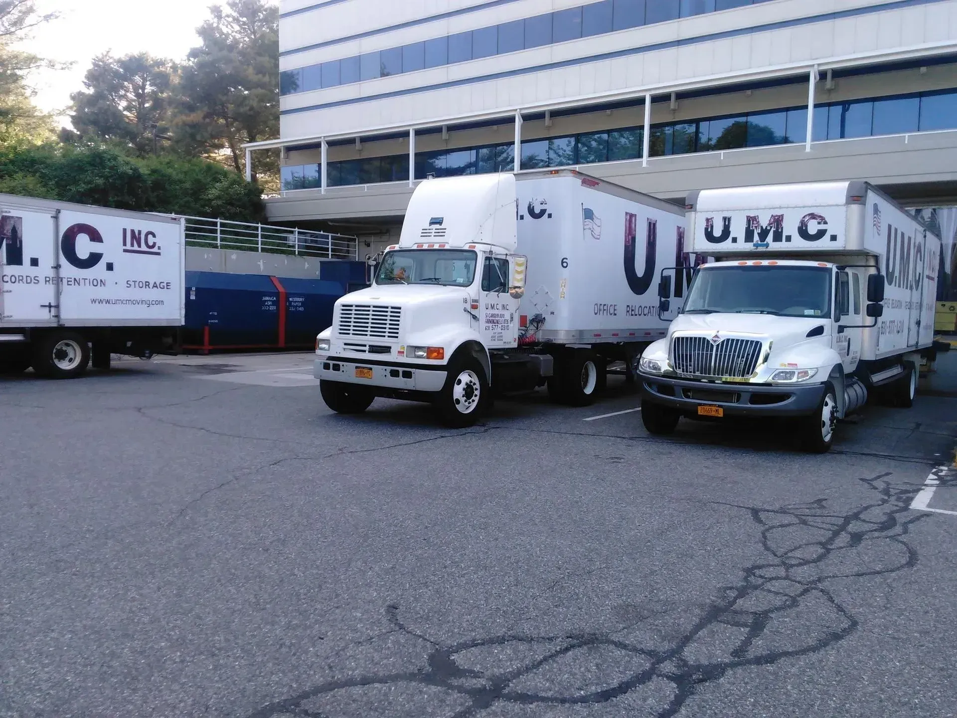 Three UMC moving trucks parked outside a building, including a white cab and a dark truck.