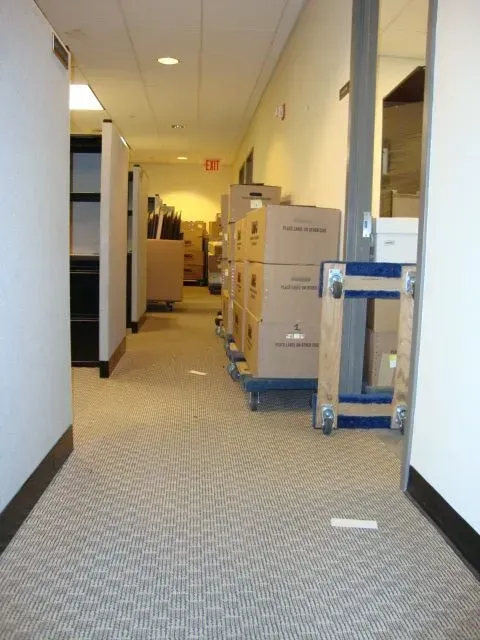 Office hallway with stacked moving boxes and carts along the right side of a carpeted corridor.