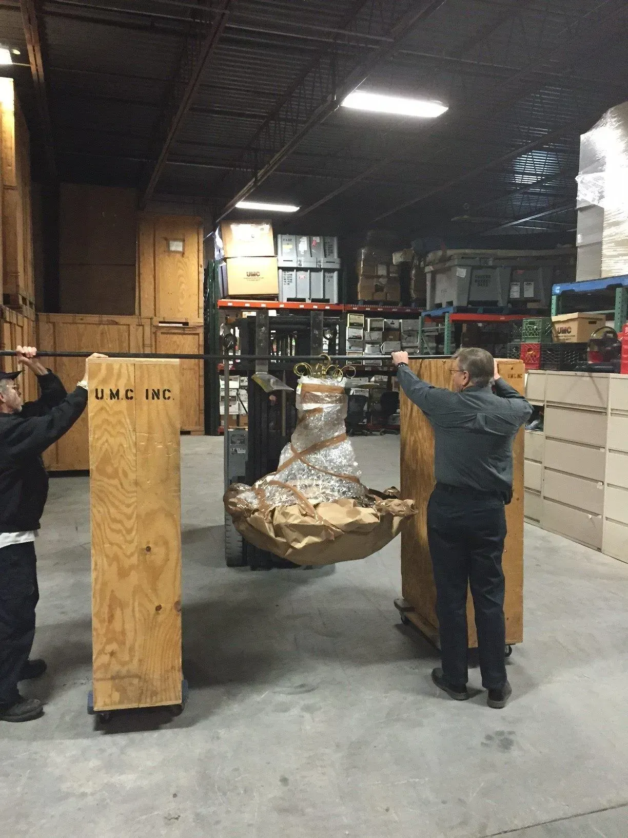 Workers moving a wrapped pallet between wooden crates in a warehouse loading area