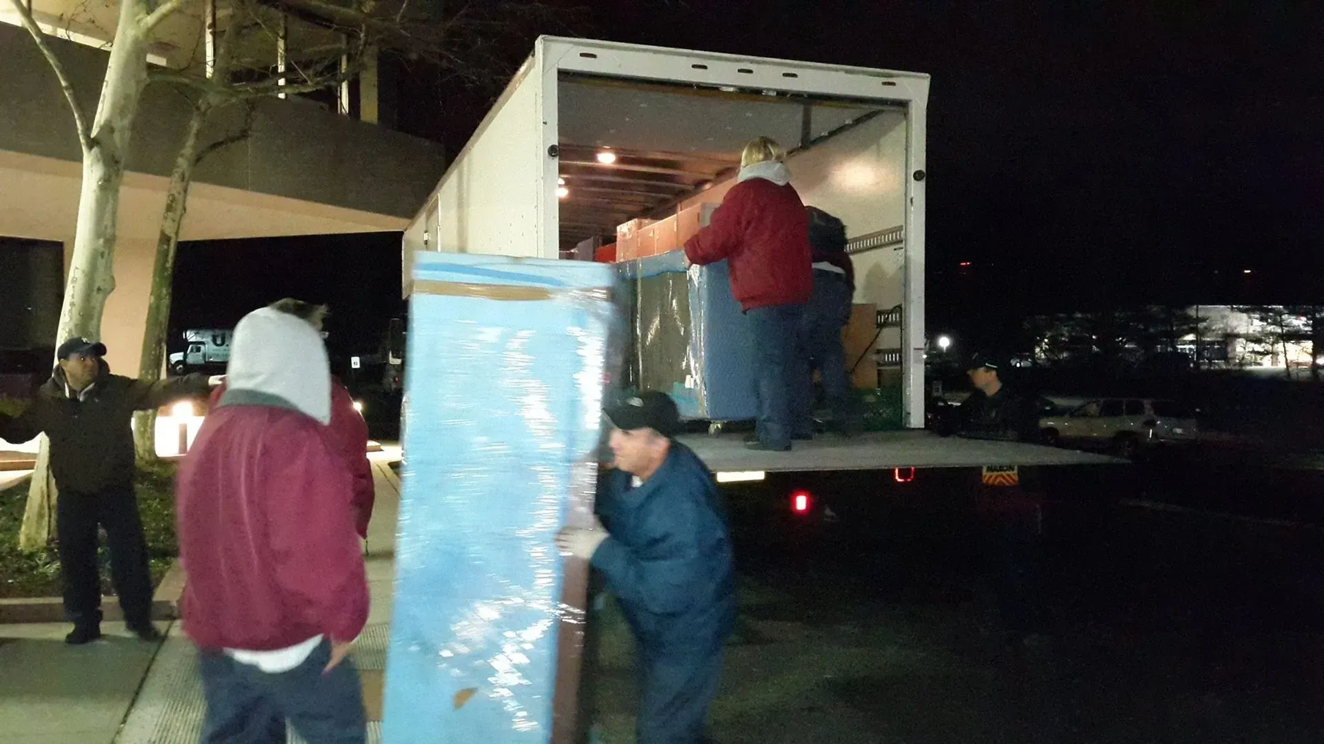 People loading furniture into a moving truck at night; one man stands on the truck, others below.