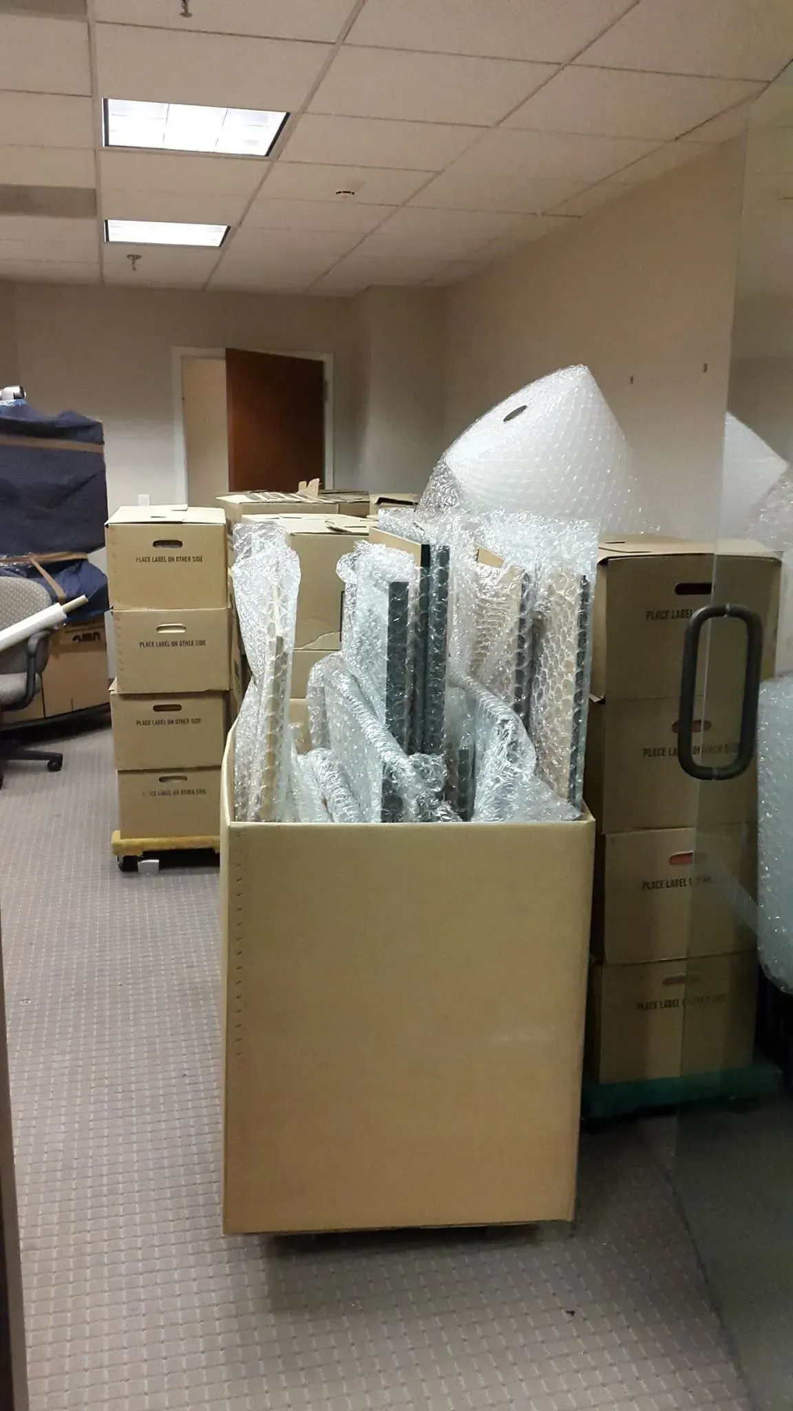 Office hallway with boxes of packed bubble wrap and filing cabinets under fluorescent lights