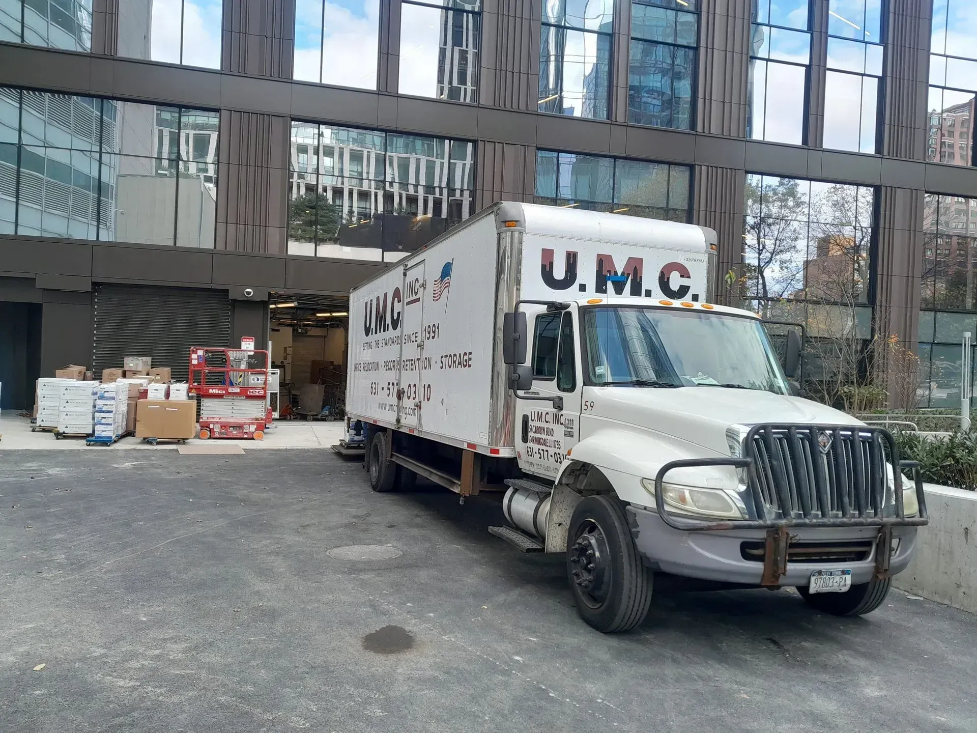 White U.M.C. box truck parked beside a glass office building in an urban lot
