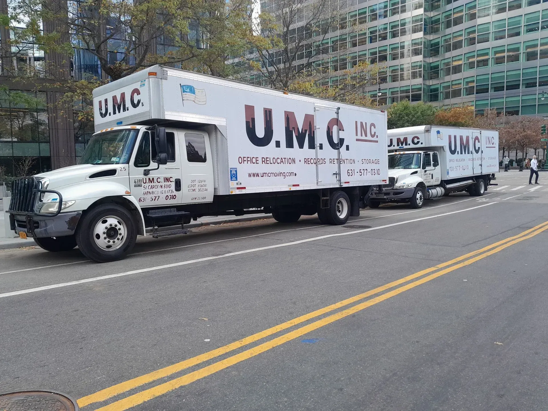 Two U.M.C. moving trucks parked along a city street, one in front of the other.